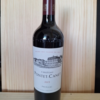 Garrafa de vinho Château Pontet-Canet 2019 com rótulo branco e cápsula vinho tinto em fundo de madeira
