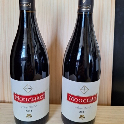 Duas garrafas de vinho tinto Mouchão 2011 com rótulo branco e vermelho sobre mesa de madeira clara