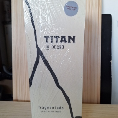 Embalagem branca de vinho Titan of Douro com linhas pretas e texto, em superfície de madeira clara.