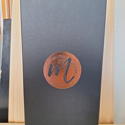 Caixa preta com selo redondo castanho e letras pretas