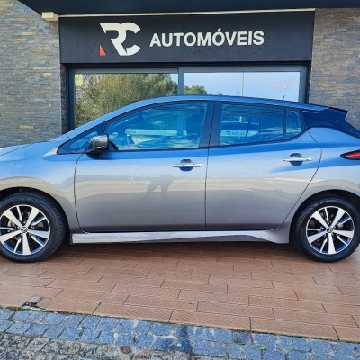 Carro cinza prateado de quatro portas em frente a loja RC Automóveis