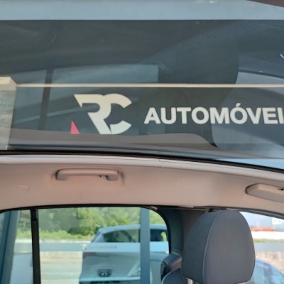 Interior de carro com teto panorâmico em vidro e banco cinza, janela com reflexo de sinalização RC AUTOMÓVEIS