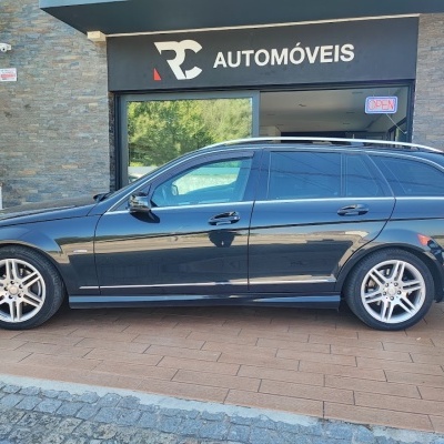 Carro preto station wagon com jantes prateadas estacionado frente a loja RC AUTOMÓVEIS