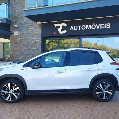 Carro branco estacionado em frente a loja RC AUTOMÓVEIS com placa OPEN.