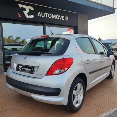 Peugeot 207 prateado estacionado junto a loja RC AUTOMÓVEIS