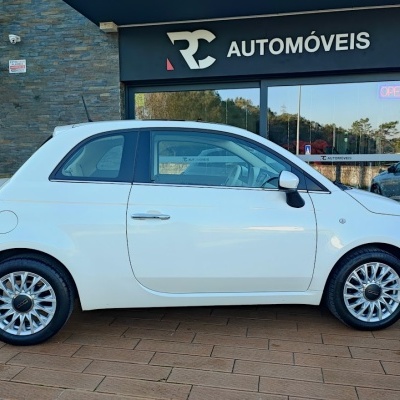Carro branco compacto Fiat 500 em frente a loja RC AUTOMÓVEIS