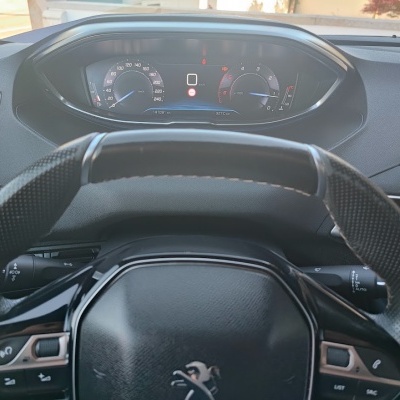 Volante preto de carro Peugeot com painel digital e odómetro visível