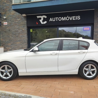 Carro BMW branco diante de loja RC Automóveis com placa OPEN