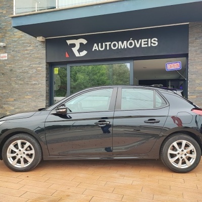 Carro preto de quatro portas em frente a loja RC AUTOMÓVEIS com placa OPEN