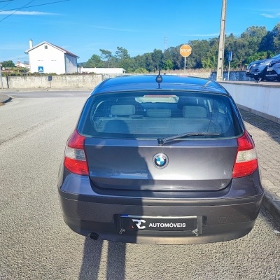 Carro BMW cinzento visto de trás com sinal STOP na rua ao fundo