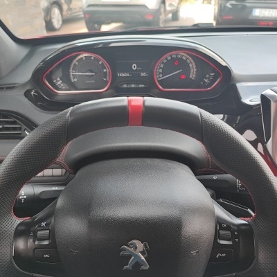 Volante Peugeot preto com detalhes vermelhos no interior de um carro