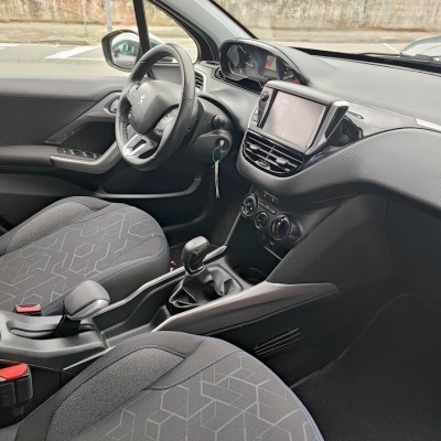 Interior de carro Peugeot com volante, bancos cinza com padrão geométrico, painel com ecrã táctil