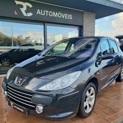 Carro Peugeot preto estacionado em frente a loja RC AUTOMÓVEIS com piso de madeira