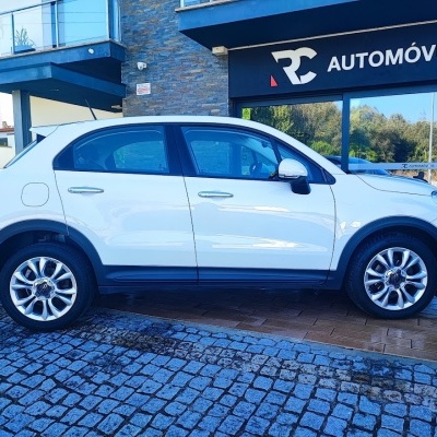 Carro branco estacionado ao lado de edifício com letreiro RC AUTOMÓVEIS