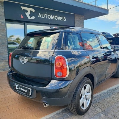Carro Mini Cooper preto de cinco portas em exterior com letreiro RC AUTOMÓVEIS