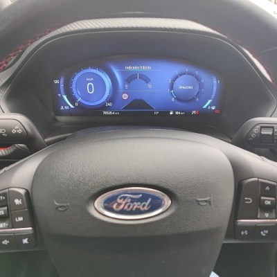 Volante Ford com painel digital azul e botões de controlo, interior de carro.