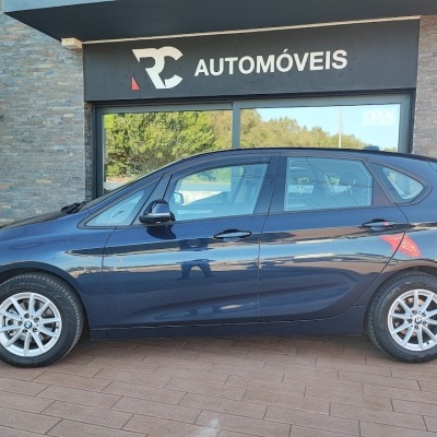 Carro hatchback BMW azul escuro em frente a loja RC AUTOMÓVEIS