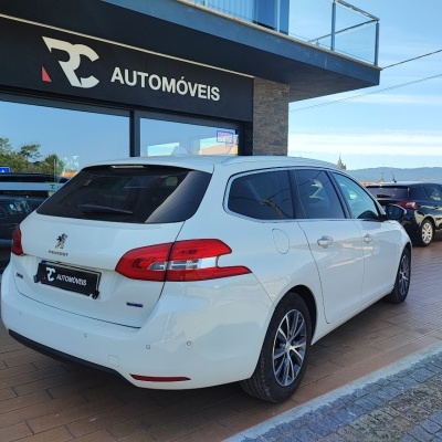 Carrinha Peugeot branca estacionada frente a loja de automóveis