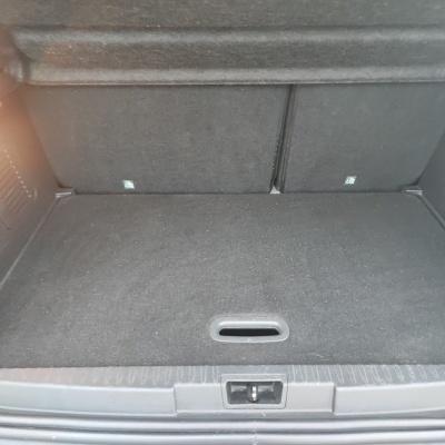 Espaço de carga de carro forrado em tecido cinzento escuro com bancos traseiros.