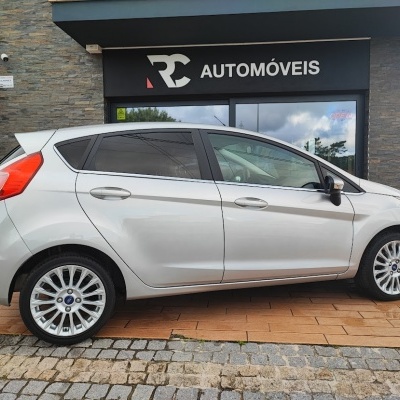 Carro prata de cinco portas estacionado em frente a loja de automóveis