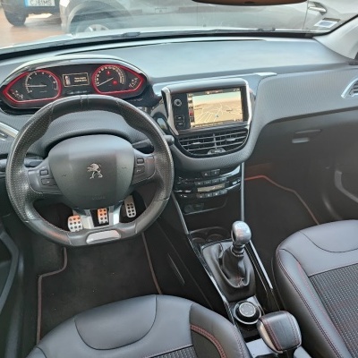 Interior de carro Peugeot com volante preto, painel com bordas vermelhas, ecrã GPS central e bancos em tecido preto