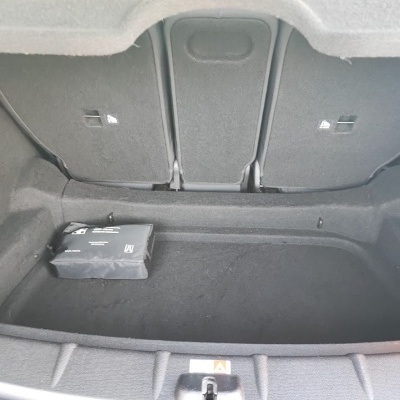 Interior da mala de um carro revestida a tecido preto com um kit de primeiros socorros preto dentro