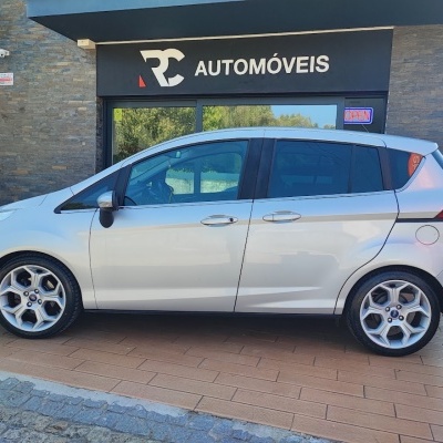 Carro prata estacionado à frente de loja RC AUTOMÓVEIS com sinal OPEN