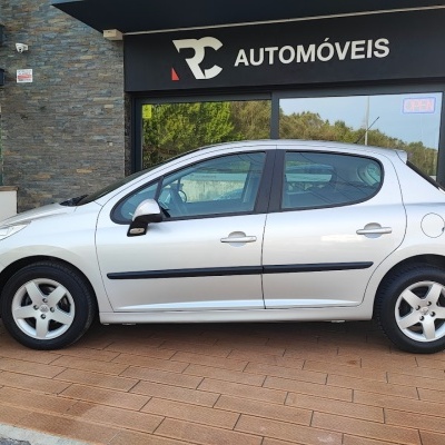 Carro citadino prata de cinco portas estacionado em frente a loja RC AUTOMÓVEIS