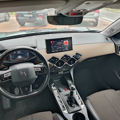 Interior de carro DS com volante preto, painel digital, ecrã central e assentos castanhos e bege