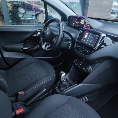 Interior carro com bancos pretos, volante Peugeot e ecrã digital no painel