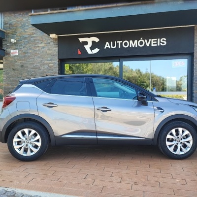 Automóvel cinza prateado com quatro portas em frente a loja RC AUTOMÓVEIS