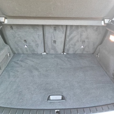 Compartimento de bagagem forrado a tecido cinzento em carro com rede lateral e luz acesa