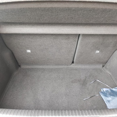 Interior de mala de carro com revestimento cinzento e saco azul no canto direito