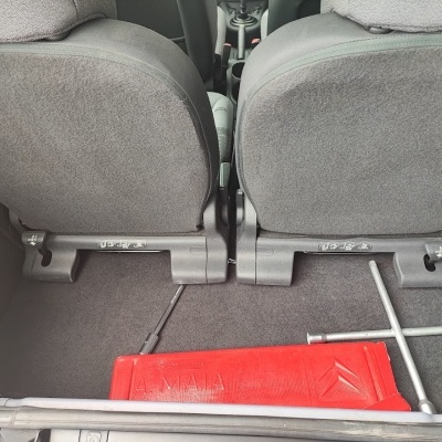 Interior da mala de carro com assentos em tecido cinza, caixa vermelha A.M.A. e chave de roda em forma de cruz