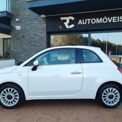 Carro citadino branco de duas portas com jantes prateadas junto a loja RC AUTOMÓVEIS