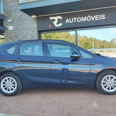 Carro azul escuro estacionado junto a uma loja com placa RC AUTOMÓVEIS e letreiro OPEN.