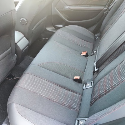 Bancos traseiros de carro em tecido cinzento com padrão e cintos de segurança.