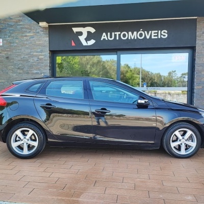 Carro preto estacionado à frente de loja RC Automóveis com sinal aberto.
