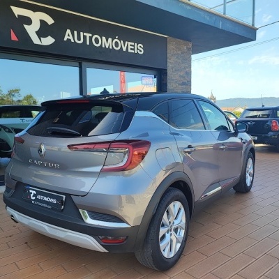 Renault Captur cinzento frente a loja RC AUTOMÓVEIS com outros carros e montanhas ao fundo