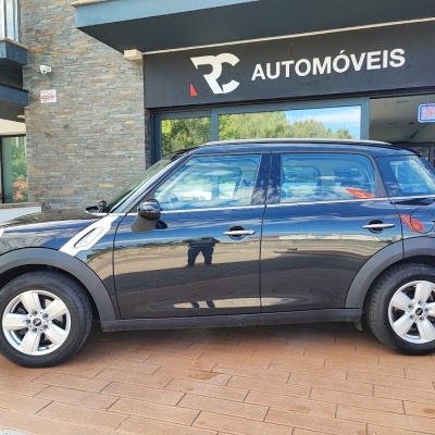Carro preto de quatro portas com letreiro RC AUTOMÓVEIS e placa OPEN na fachada