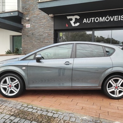 Carro cinza metálico estacionado à frente de loja com letreiro PRE AUTOMÓVEIS e placa neon OPEN