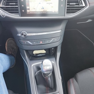 Interior do carro com painel central cinzento, ecrã tátil a mostrar mapa, alavanca de velocidades manual e bancos com costura vermelha