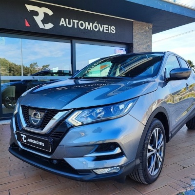 Carro Nissan cinza metálico estacionado em frente a loja RC AUTOMÓVEIS