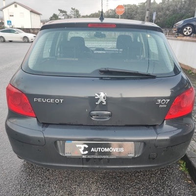 Peugeot 307 HDI cinzento visto de trás num passeio urbano molhado