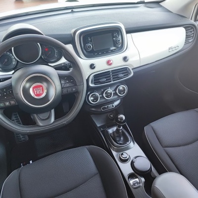 Interior de carro FIAT 500 com volante, assentos em tecido escuro e painel em preto e branco.
