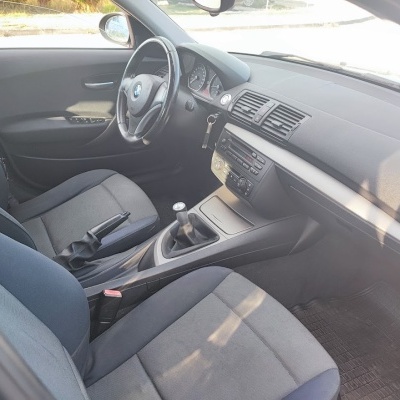 Interior de carro BMW com bancos de tecido cinza e detalhes azuis, volante preto, e painel com botões