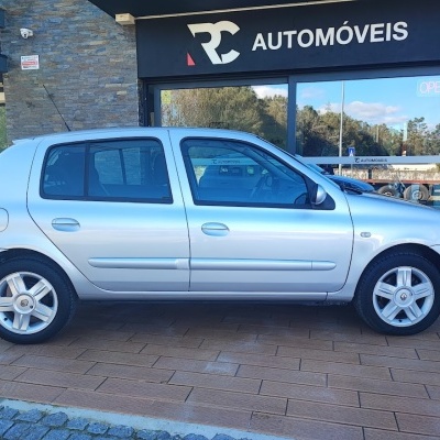 Carro prateado de quatro portas à frente de loja RC AUTOMÓVEIS com sinal OPEN