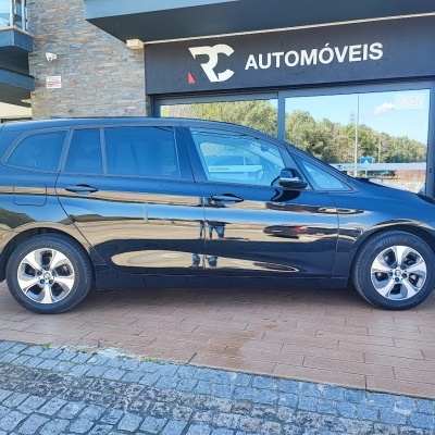 Carro familiar preto com vidros escurecidos estacionado em frente a uma loja de automóveis