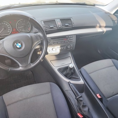 Interior do carro BMW com volante de couro, painel cinza, rádio, bancos em tecido cinza e azul, caixa de câmbio manual.