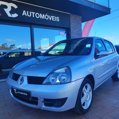 Carro Renault prata junto a loja RC AUTOMÓVEIS com sinal OPEN
